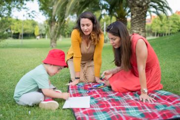 A child and two women enjoying a drawing session on a picnic blanket in a park in Portugal.