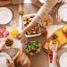 Overhead view of a diverse cheese platter setup for a delicious meal, featuring fresh produce and juices on a table.